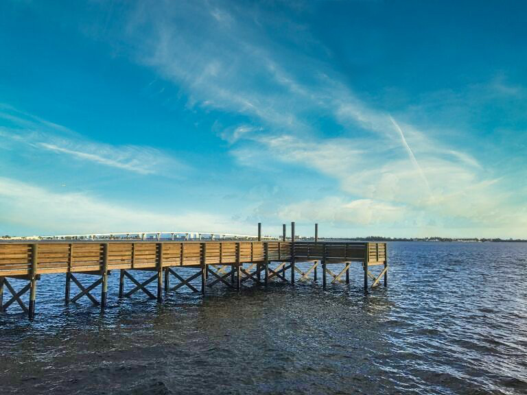 Wooden boat dock extending into the Indian River Lagoon in St. Lucie County, Florida, under blue sky and scattered clouds.