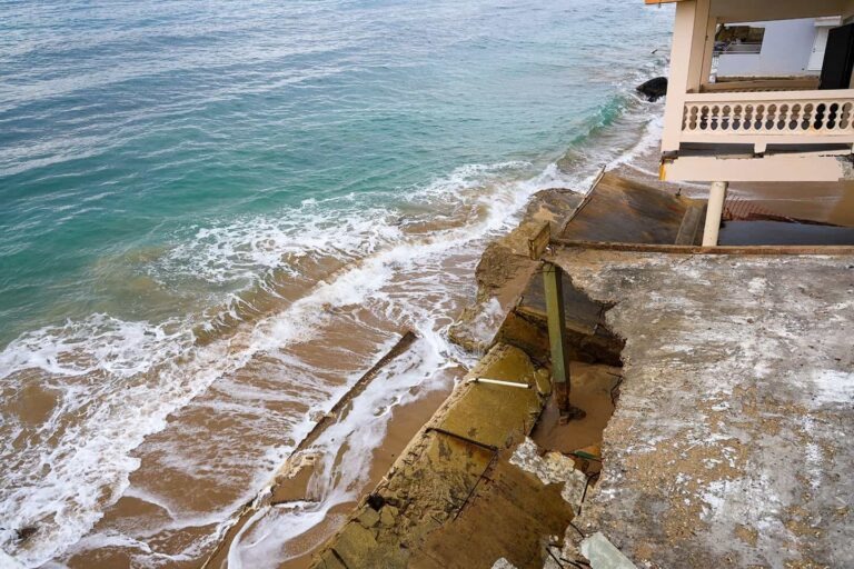 Coastal building with severe structural damage due to erosion and ocean waves, with collapsed concrete slabs on the shoreline