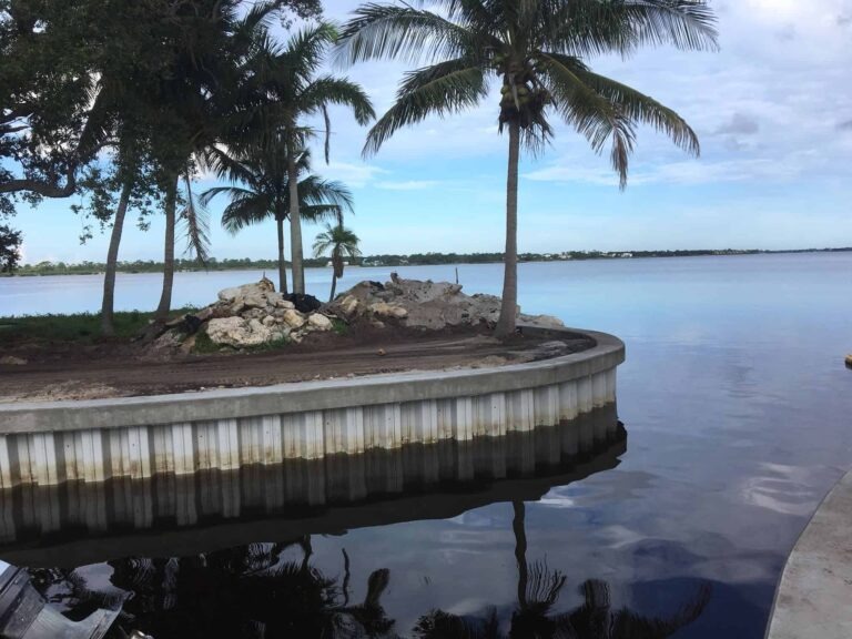 Curved vinyl seawall with palm trees and shoreline under construction along a calm waterfront