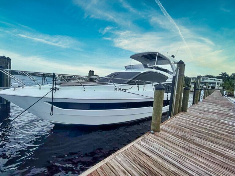 Luxury white yacht docked at a wooden marina pier on a cloudy day, with waterfront homes in the background