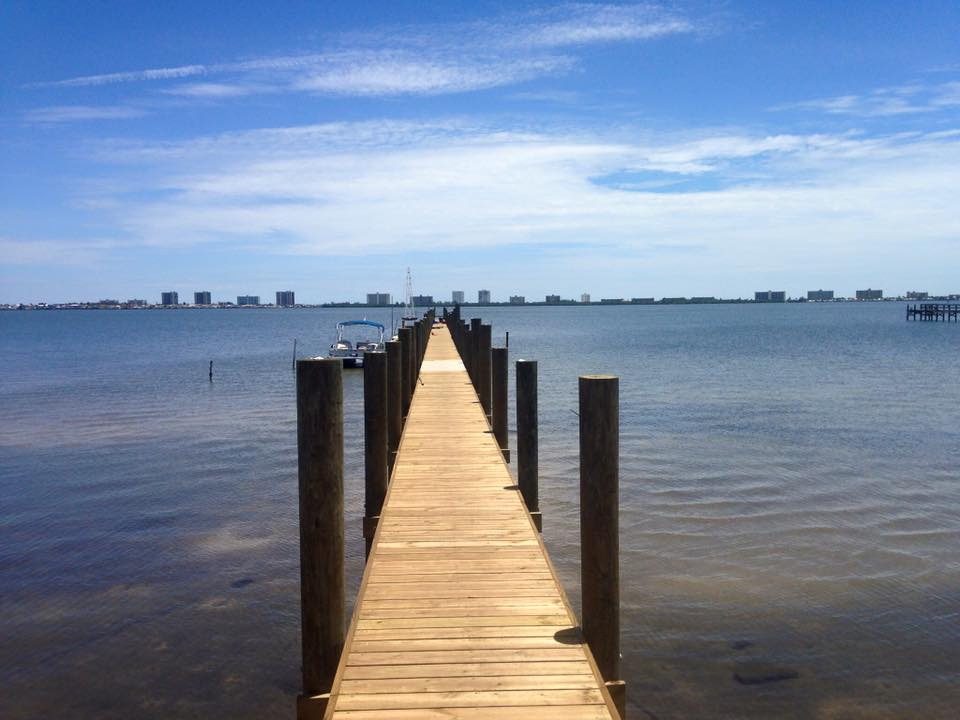 Long wooden pier extending over calm bay waters toward distant high-rise condominiums