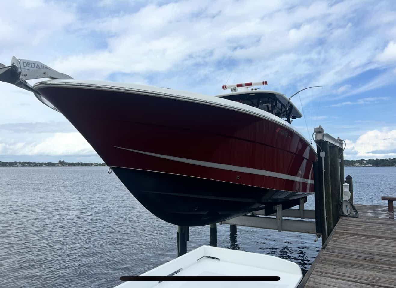 Large red and white powerboat lifted on a boat hoist next to a wooden dock over calm coastal waters.