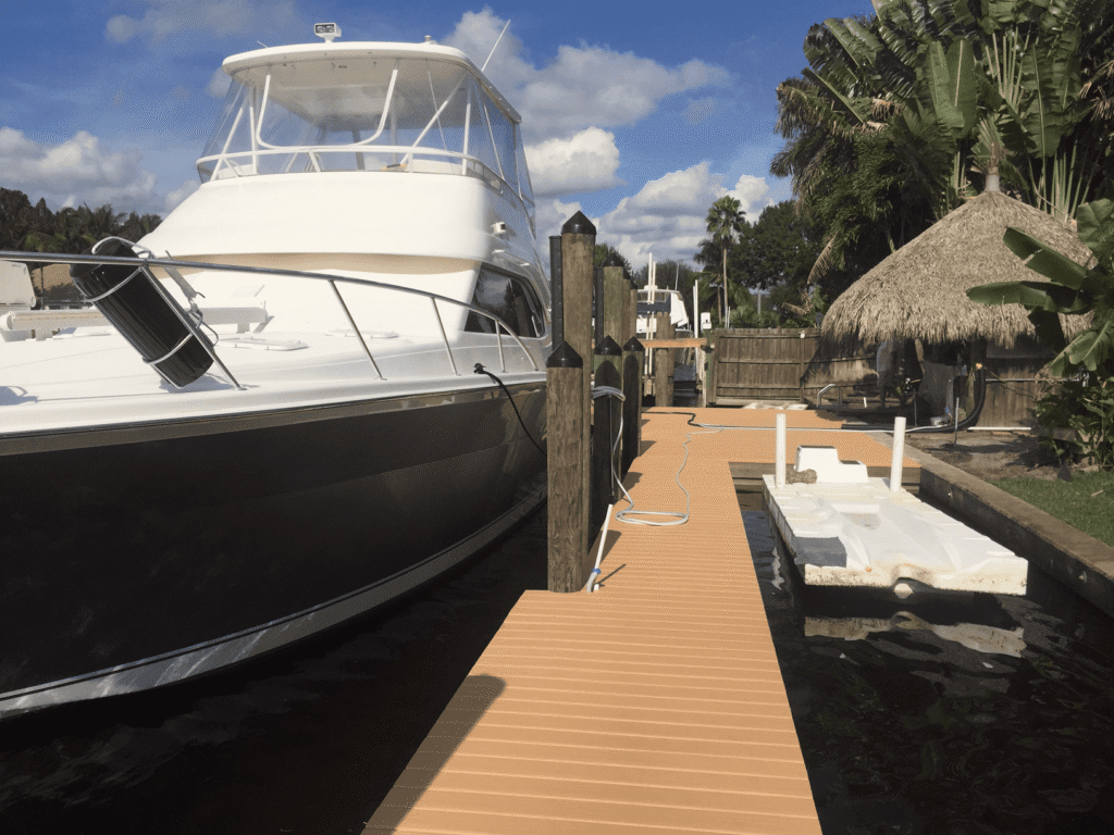 Large yacht docked at a private residential pier with floating jet ski lift and tiki hut in background