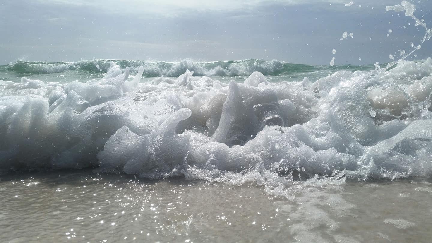 Close-up of foamy ocean waves crashing onto a sandy shoreline under a cloudy sky