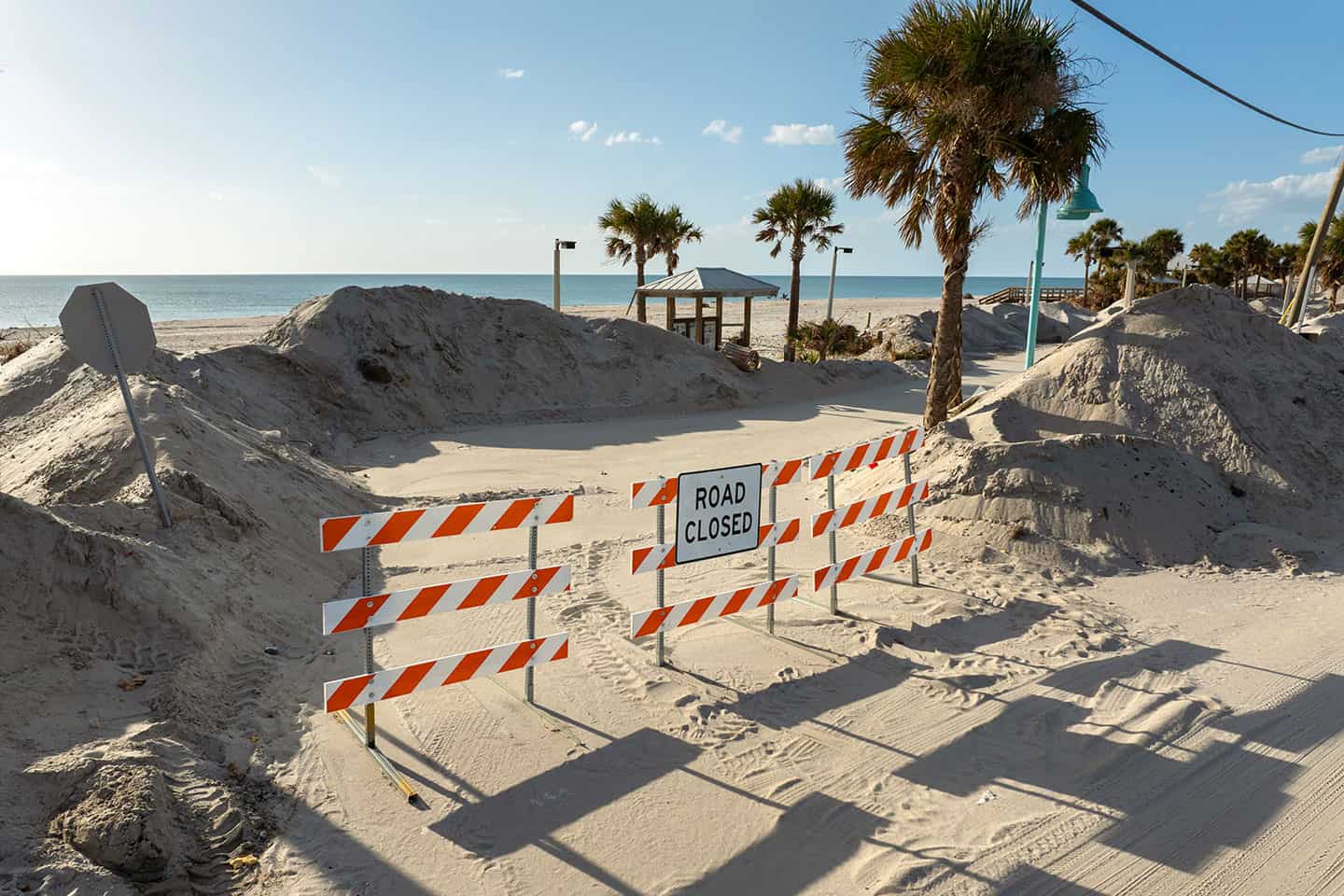 Road closed sign blocking sandy beach access after coastal erosion or storm damage