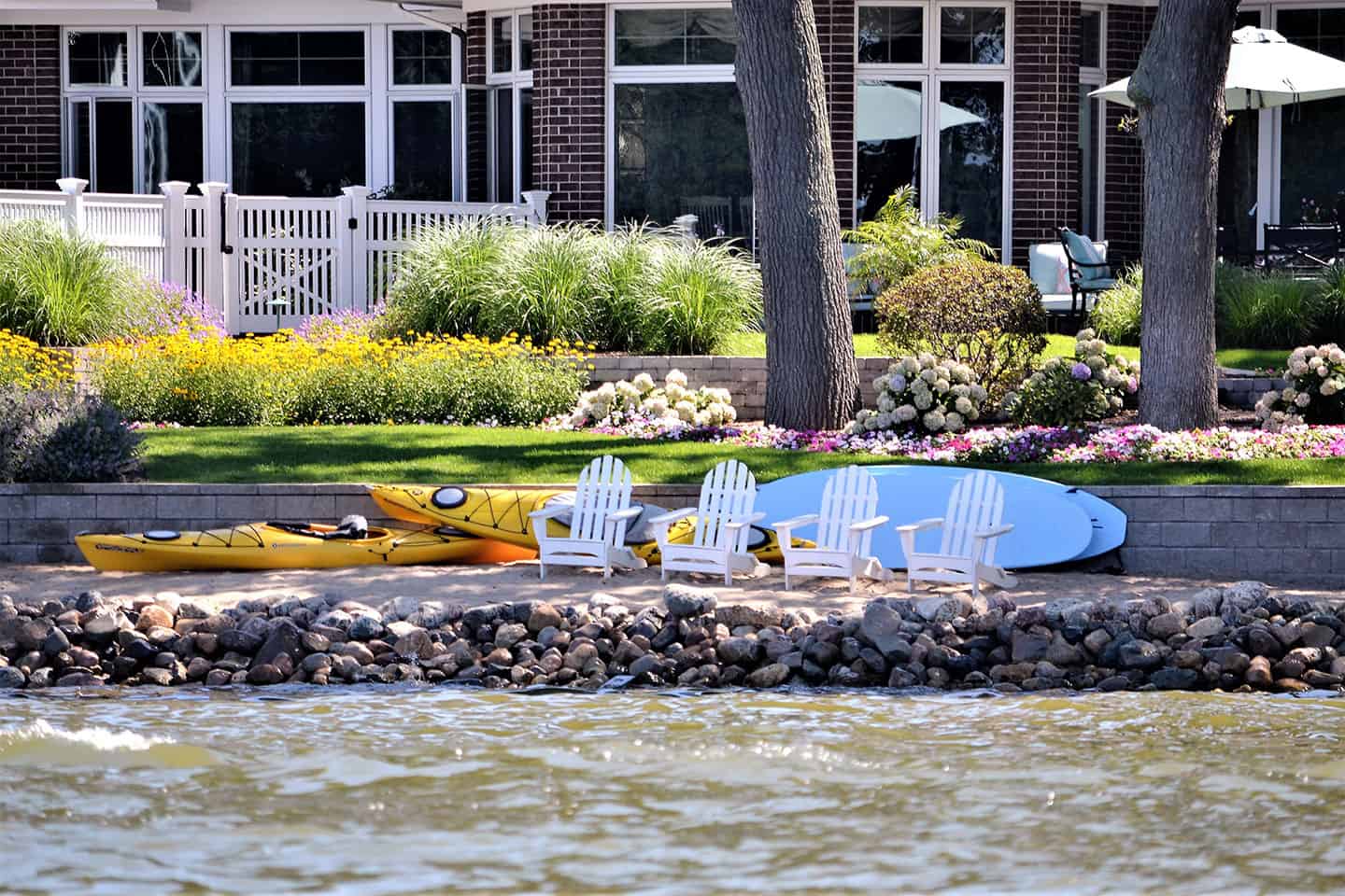 Waterfront backyard with Adirondack chairs, kayaks, and paddleboards by a stone seawall