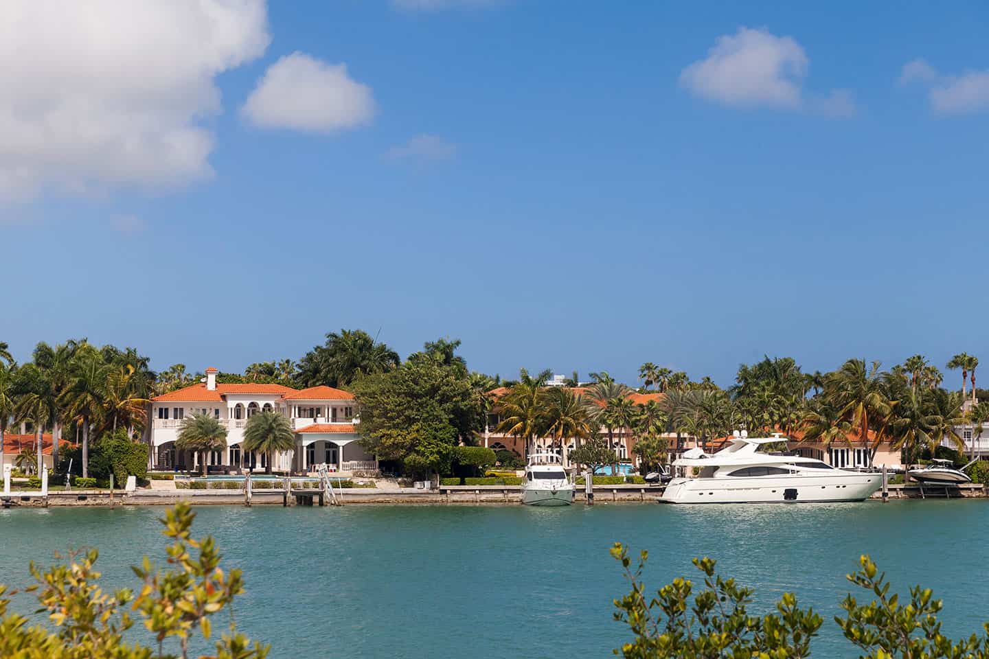 Luxury waterfront homes with red tile roofs and docked yachts on a sunny day