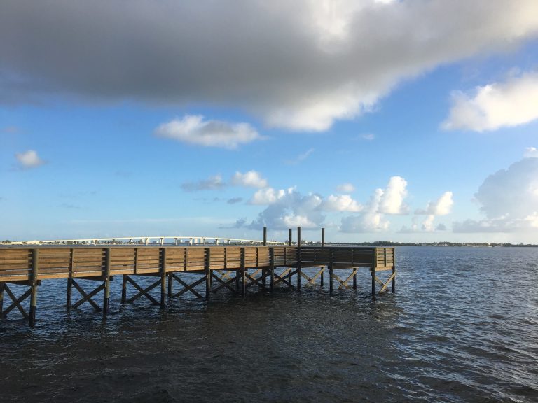 Wooden boat dock extending into the Indian River Lagoon in St. Lucie County, Florida, under blue sky and scattered clouds.